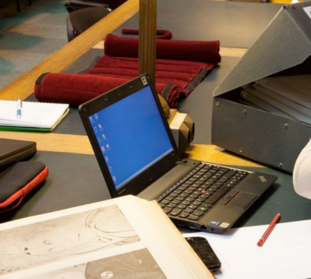 Ordinateur portable sur une table et archiviste qui fait une recherche dans des dossiers