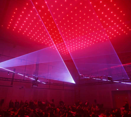 Public assis à terre observant des jeux de lumières. Dominante rouge très forte.