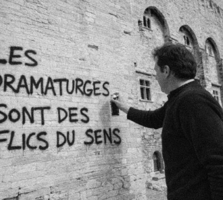 Homme peignant à la bombe le texte suivant sur un mûr de pierre : "les dramaturges sont des flics du sens"