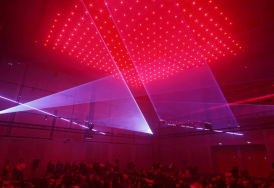 Public assis à terre observant des jeux de lumières. Dominante rouge très forte.