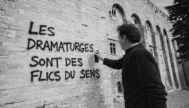 Homme peignant à la bombe le texte suivant sur un mûr de pierre : "les dramaturges sont des flics du sens"