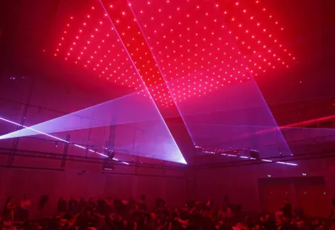 Public assis à terre observant des jeux de lumières. Dominante rouge très forte.