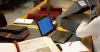 Ordinateur portable sur une table et archiviste qui fait une recherche dans des dossiers