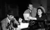 extrait d'un film en noir et blanc où l'on voit une femme et deux hommes autour d'une machine à écrire